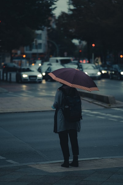 白天站在人行道上的一名身穿黑色外套、手持雨伞的妇女